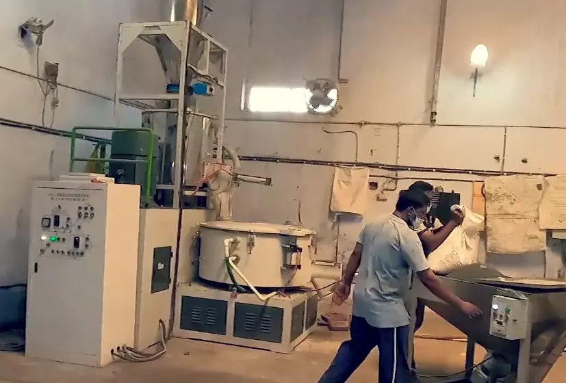 Two men load raw materials into the funnel of a PVC Water Stopper manufacturing machine in a factory